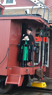 Two women in Victorian era reproduction clothing stand on back of White River Lumber Co caboose.