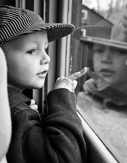 Birthday boy enjoying train ride. Child looks out window of train with his reflection captured in window.