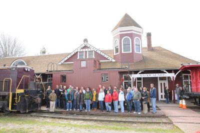 Group gather along side caboose parked in front of Snoqualmie Depot