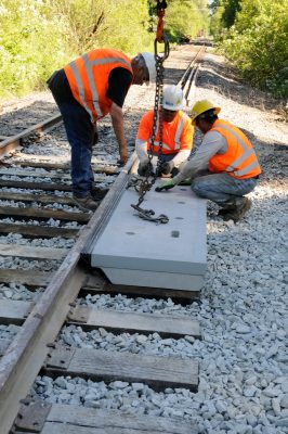 New concrete crossing panel is lowered into place. Large lag screws driven into the white oak cross ties will hold them in place.