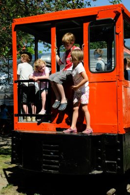 Children climb on and in the cab of the orange Whitcomb locomotive at the Snoqualmie Depot grounds