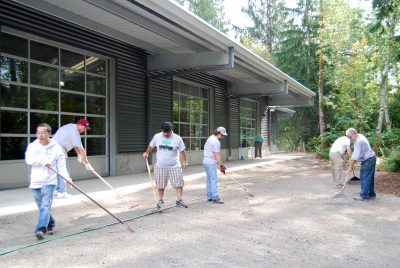 Microsoft volunteers raking gravel at the Train Shed, another volunteer is washing windows behind them.