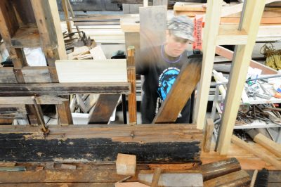 A crewmember is installing new framework to the Chapel Car. Both new wood and old wood are visible, along with missing sections to be replaced.