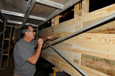 Worker installs screws into replacement framework on the Chapel Car. Framework appears complete.