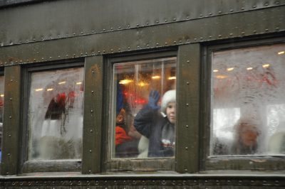 A picture of the side of Spokane, Portland & Seattle 276. Three windows are visible. The middle window has a child with a Santa hat, hand against the window, intensely looking outside. The other two windows are cloudy with condensation.