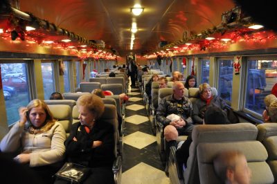 People sit in 1950's reclining coach chairs aboard an antique railroad coach, Spokane, Portland & Seattle 276. Christmas decorations are hanging from the baggage racks and sides of the car.