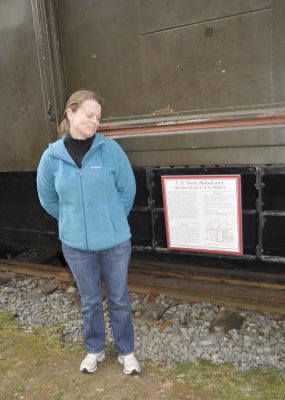 Educator Jessie Cunningham stands next to an informational sign attached to the Army Ambulance Kitchen Car. The sign is affixed to the ladder below the central sliding door