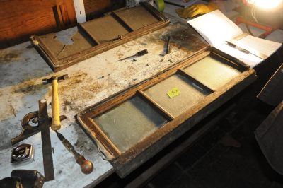 Messenger of Peace clearstory windows sit on a desk. Old shellac, hardware, and glass is removed.