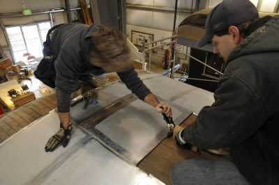 Two sheet metal specialests slide new Terne II roof panels into place on Messenger of Peace.