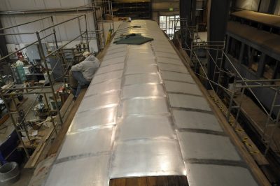 New panels of Terne II roofing being installed on the roof of Messenger of Peace. A worker sits on the lower level of the roof.