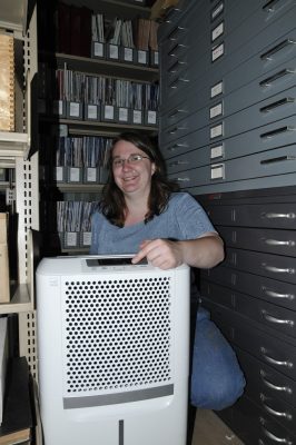 Cristy L. with a new dehumidifier in the museum's periodical and drawing storage area.