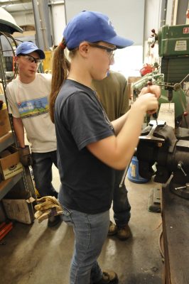 A 2012 RailCamper taps a hole drilled in a slice of rail in the CRW. Other RailCampers look on.