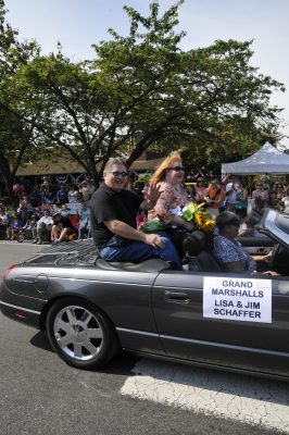 Lisa and Jim Schaffer ride on the back of a convertible car as Grand Marshalls of Snoqualmie Railroad Days 2012. Paradegoers and the Snoqualmie Depot can be seen in the background.