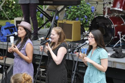 Three singers for Brian Vogan & his Good Buddies sing in front of the Skagit Flatcar Stage at the Snoqualmie Depot during Snoqualmie Railroad Days 2012. Other members of the band can be seen on the flatcar behind them.