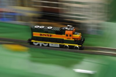 A LEGO BNSF locomotive speeds down the track. The locomotive is in focus, but the rest of the background is blurry, suggesting speed.