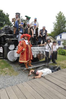 Seafair Pirates pose for a picture on the front of US Plywood locomotive #11. One pirate lies across the tracks in front of #11.