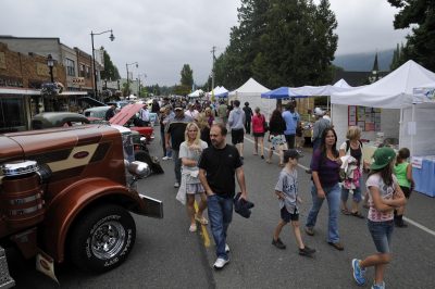 A crowd of people walk along Railroad Ave. during Snoqualmie Railroad Days 2012. On the right (south) side, vendor booths line the street; on the left (north) side, cars line the street as part of a car show.