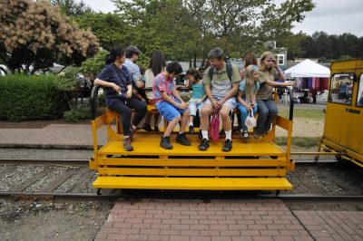 Visitors sit aboard the Museum's speeder trailer for rides during Snoqualmie Railroad Days 2012. Vendor stalls can be seen along Railroad Ave. behind them.