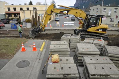 Concrete crossing panels are stacked at the Main Ave. S crossing in North Bend. Behind, an excavator grades the trackless crossing.