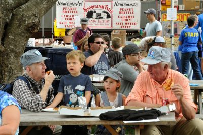 Families and staff eat at picnic tables with a Snoqualmie Falls Candy Company booth behind during DOWT 2014.