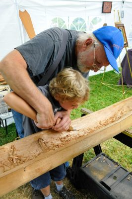 A master carver helps a young visitor learn how to carve a canoe at SRD 2014.