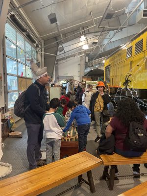 Young visitors play with train tables in the Train Shed. There are Halloween decorations present, and some costumes visible.