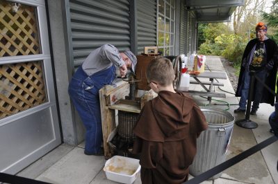 Earl W. running his cider press during Halloween Train 2024 while guests look on.