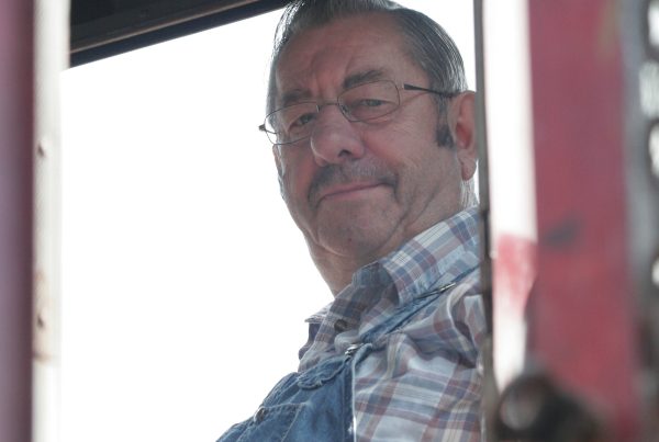 Volunteer Vern S. in the cab of one of the Museum's locomotives. The photo is taken from the ground looking through the end door, and Vern is smiling at the camera.