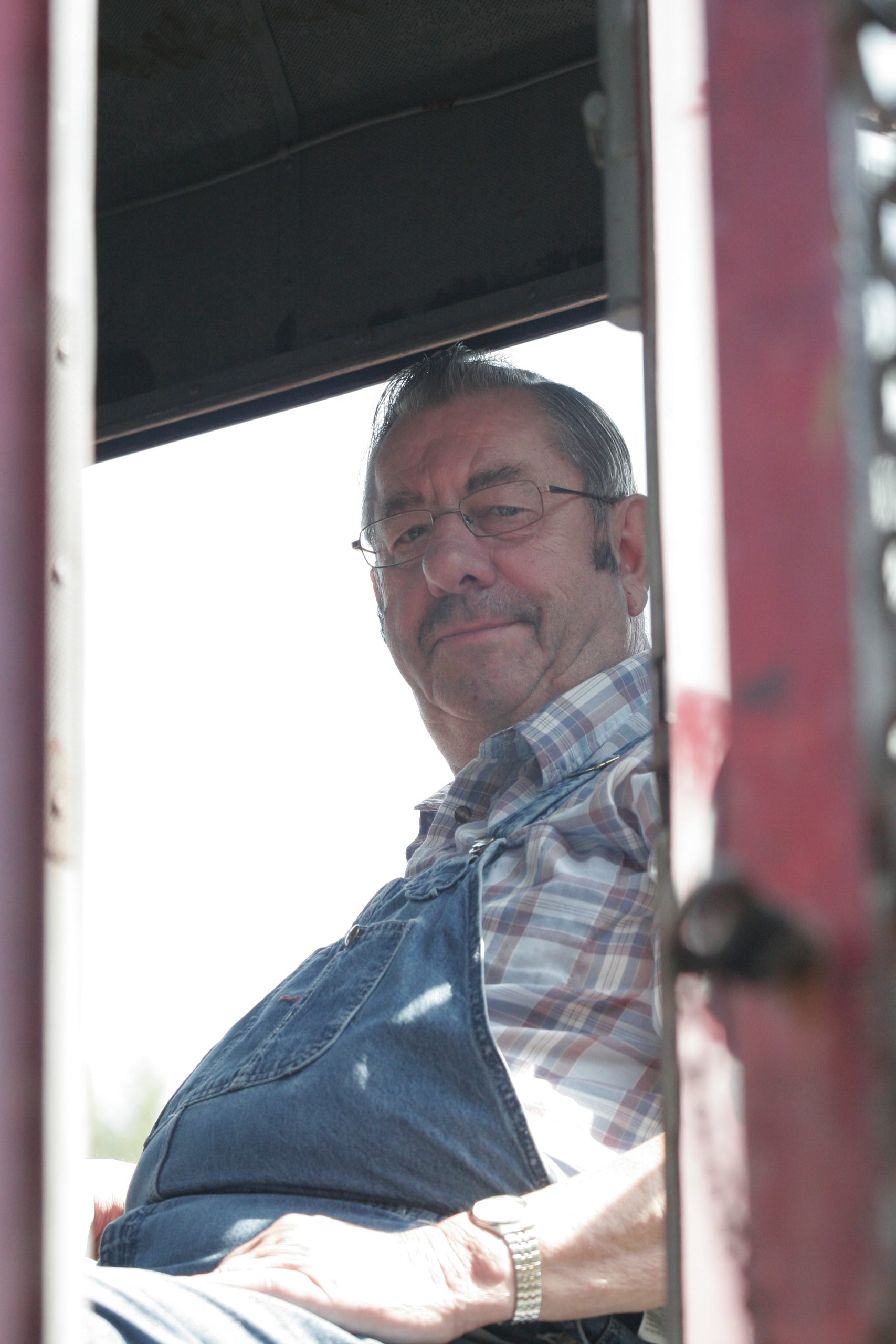 Volunteer Vern S. in the cab of one of the Museum's locomotives. The photo is taken from the ground looking through the end door, and Vern is smiling at the camera.