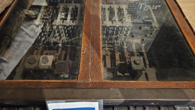 The top of a large wooden cabinet with glass panels. Inside, old electronic relays and levers are visible.