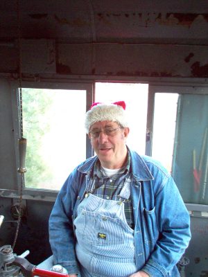 Vern S. in the cab of one of the Museum's locomotives during Santa Train 2004. Vern is seated in the Engineer's seat and is wearing a "Santa" hat with his Engineer outfit.