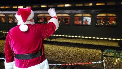 Santa waving to the departing train, everything lit with warm lights in the dark.