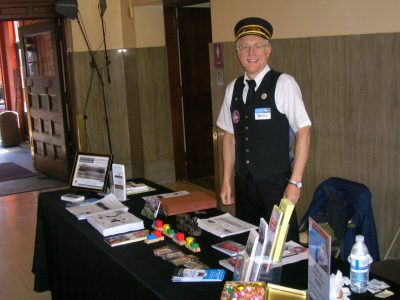 Volunteer and Board Member Dennis S. standing behind a table with brochures and giveaways inside Portland Union Station during National Train Day 2010.