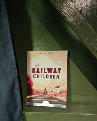 The Railway Children book sitting in a green background with blue fabric hanging to the left.