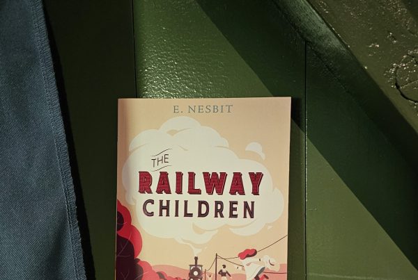 The Railway Children book sitting in a green background with blue fabric hanging to the left.