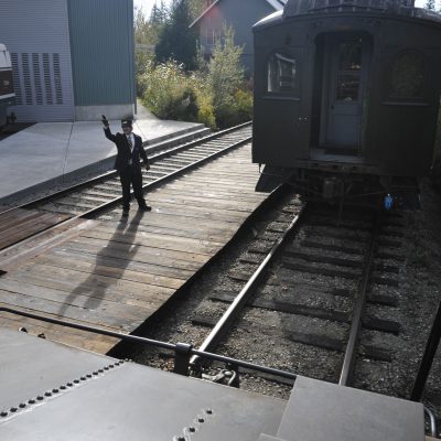 A Conductor controlling switching operations at the RHC. The Conductor is standing on the platform, with a wooden coach behind the tender of a locomotive.