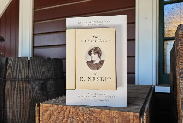 A book title "The life and Loves of E. Nesbit" displayed atop a wooden box. An old barrel is to its left, and the side of the Snoqualmie Depot is behind it.