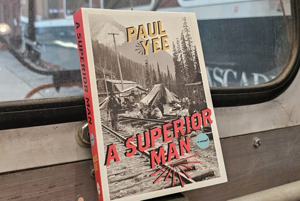 The book "A Superior Man" by Paul Yee rests on the front of a motor car. Through the windows can be seen the Museum's Amtrak Talgo Bistro Car and Northern Pacific Tool Car