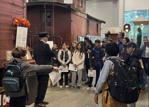 A group of students listen to a volunteer presentation during a field trip.