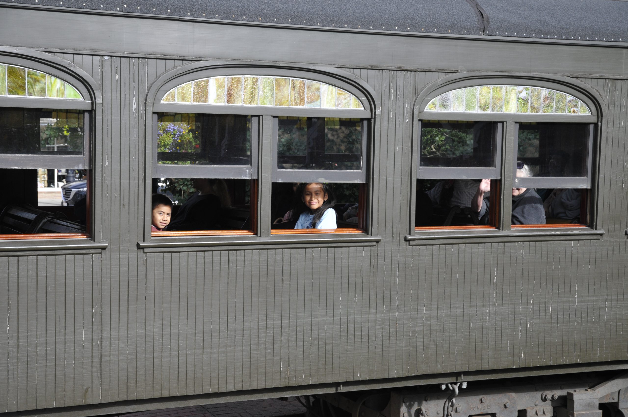 Two visiting children smile at the camera as the train passes by.