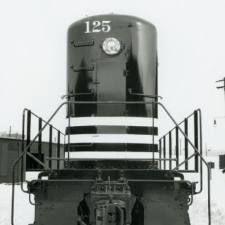 Historic builder's photo of NP Locomotive 125 from the front. It is solid black with three bold, white stripes that wrap around the front of the hood.