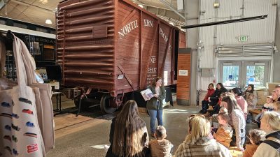 A Museum educator reads to parents and their young kids in the Train Shed Exhibit Hall.