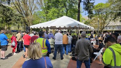 People crowd around a tent in Holladay Park in Portland. TriMet officials and workers talk about the retiring Type 1 LRVs. LRV 124 can be seen in the distance to the left.