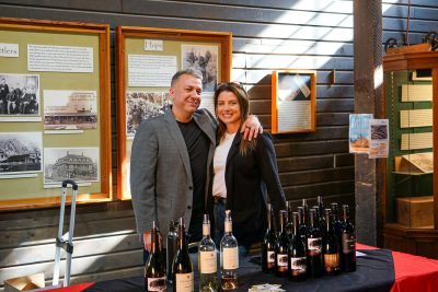 Two winery employees pos for a picture in the Snoqualmie Depot freight room. Wines from their winery stand on the table in front of them.