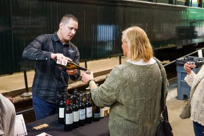 A winery employee pours wine for a Wine Train guest in front of Chapel Car Messenger of Peace.